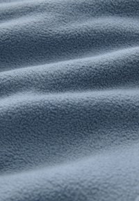 Jasnoniebieski polar z miękką, kręconą fakturą i delikatnymi fałdami tworzącymi subtelne cienie na powierzchni.