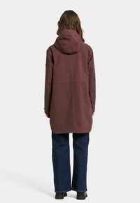 Bordeaux waterdichte jas met een capuchon, met een rechte snit, lange mouwen en zijzakken. Gecombineerd met donkere jeans en zwarte laarzen.