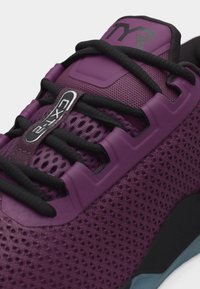 Μωβ αθλητικό παπούτσι με μαύρα κορδόνια, άνω μέρος από δίχτυ και ετικέτα "CX-12" στη γλώσσα κοντά στην περιοχή των κορδονιών.