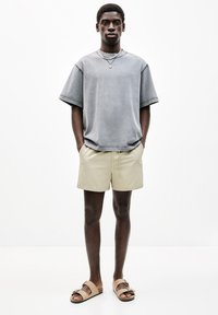 Graues, übergroßes Baumwoll-T-Shirt, beige Shorts und braune Sandalen. Einfaches Design mit lockerer Passform und minimalen Nähdetails.