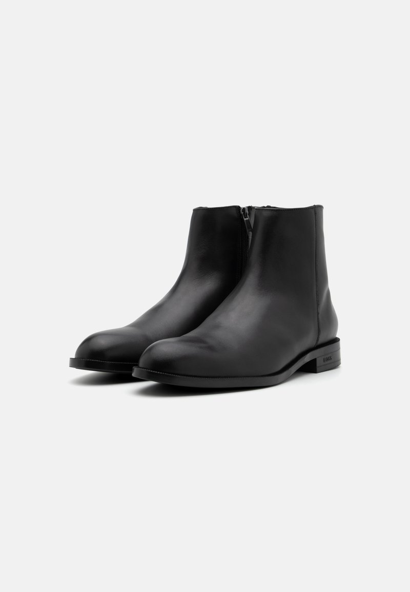 Bottines noires en cuir avec une texture lisse, bout arrondi et fermeture éclair sur le côté. Semelle robuste avec un design minimaliste et un détail logo discret.