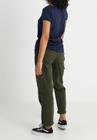 T-shirt bleu marine à manches courtes associé à un pantalon cargo vert olive, avec des poches latérales et des ourlets retroussés, porté avec des baskets noires.