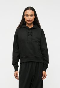 Μαύρη φούτερ με κουκούλα και μπροστινή τσέπη, με διακριτό λογότυπο στο στήθος, κατασκευασμένη από μαλακό ύφασμα με άνετη εφαρμογή και ριμπ μανσέτες.