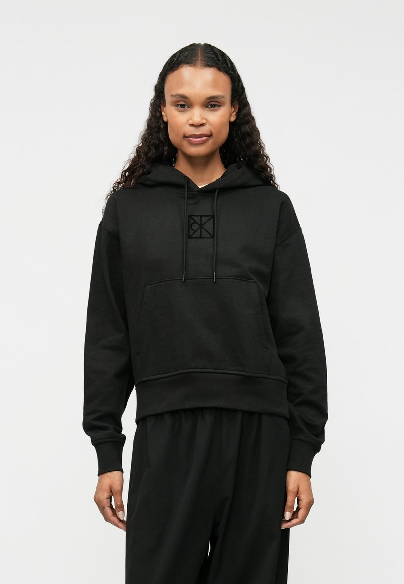 Μαύρη φούτερ με κουκούλα και μπροστινή τσέπη, με διακριτό λογότυπο στο στήθος, κατασκευασμένη από μαλακό ύφασμα με άνετη εφαρμογή και ριμπ μανσέτες.