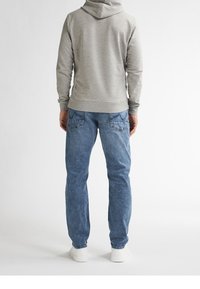 Felpa grigia in pile con cappuccio, indossata su jeans di denim azzurri chiari, con tasche posteriori e sneaker bianche.