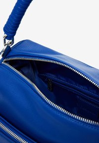 Blaues Lederhandtasche mit strukturiertem Außenmaterial, Reißverschlussfächern und einem gewickelten Griff. Das Innere verfügt über ein glattes Futter und eine kleine Tasche.