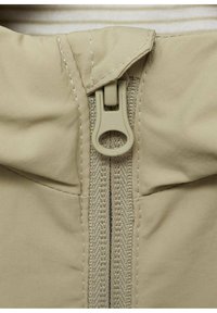 Tessuto beige con zip e superficie testurizzata. La zip è in plastica con un gancio per aprirla, posizionata al centro anteriore, accentuata da cuciture visibili.