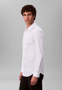 Valge pika varrukaga särk, mis on valmistatud siledast kangast, omades klassikalist kraed ja kõverat alaosa, kantud tumedate pükstega.