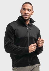 Schwarze Fleecejacke mit durchgehendem Reißverschluss, hohem Kragen und kontrastierendem glattem Stoff im oberen Bereich. Verfügt über ein Logo und strukturierte Ärmel.