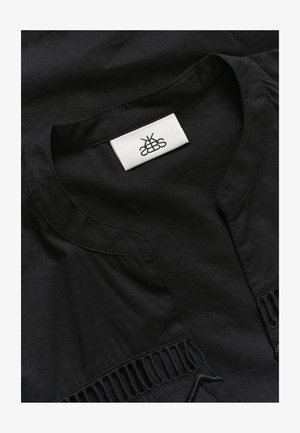 Mustast riidest rõivas, millel on ümar kaelus, õrnad voldid külgedel ning kangasilt keskel logo järgi. Pehme tekstuur.