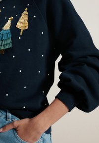 Felpa blu navy con pois bianchi, ornata da alberi ricamati in verde e oro, e polsini a costine. Morbido al tatto, vestibilità casual.