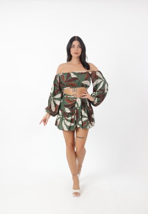 Off-shoulder twee-delige outfit met groene stof voorzien van grote witte en bruine bladerenpatronen, pofmouwen en een flared rok.