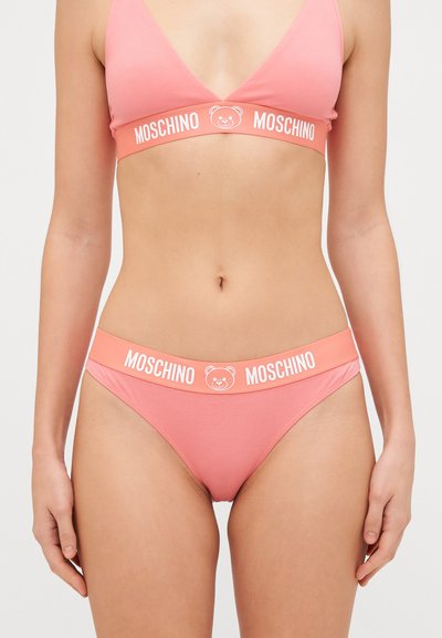 Vaaleanpunainen puuvillabralette ja siihen sopivat alushousut, joissa on karhulogo ja valkoinen "MOSCHINO"-teksti vyötäröllä. Mallissa on yksinkertainen ja sileä muotoilu.