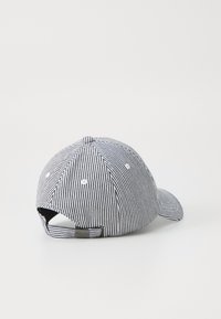Striped baseball cap in black and white, featuring a curved brim, six-panel design, ventilation eyelets, and an adjustable strap at the back.