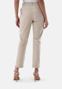 Beige maßgeschneiderte Hosen mit glatter Textur, zwei Gesäßtaschen und geraden Beinen, kombiniert mit nudefarbenen High-Heels.