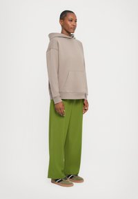 Sweat-shirt à capuche gris avec poche kangourou, associé à un pantalon ample vert clair et des baskets vert olive avec des rayures noires.