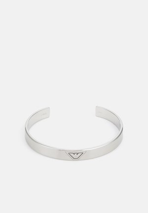 Sølvmetall mansjettarmbånd med en jevn finish, med et trekantet logoaksent i midten. Åpne ender for justerbar størrelse.