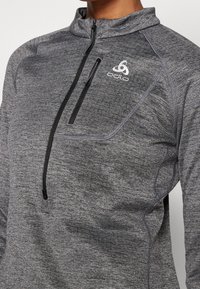 Grå kvartslång zip-pullover tillverkad av texturerad tyg, med en zip-ficka på bröstet och en vit logotyp på vänster bröst.