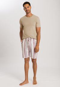 Pánský outfit se skládá z dobře padnoucího béžového trička s krátkým rukávem a vzorovaných šortek s červenými a bílými vertikálními pruhy, elastickým pasem a šňůrkou.