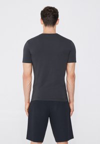 Camiseta de manga corta, de color gris oscuro, con cuello redondo, textura suave y diseño ajustado, combinada con pantalones cortos oscuros.