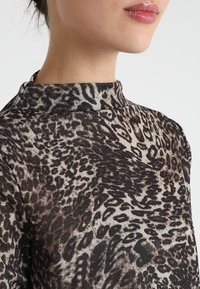 Tight passform med hög krage, tillverkad av mjukt tyg i leopardmönster med bruna och svarta nyanser, subtila glittrande texturdetailler.