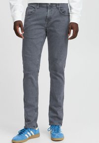 Vaqueros de mezclilla gris con un ajuste slim, que presentan bolsillos frontales, detalles de costura sutiles y un cierre de cremallera. Combinados con zapatillas deportivas azul claro.