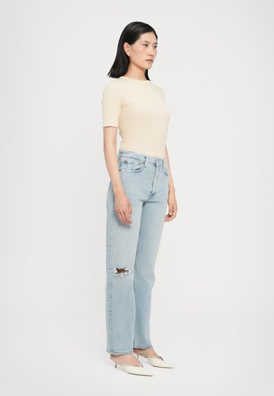 Light beige fitted top, light blue high-waisted jeans with a distressed knee, and white heeled mules. Simple and contemporary design.