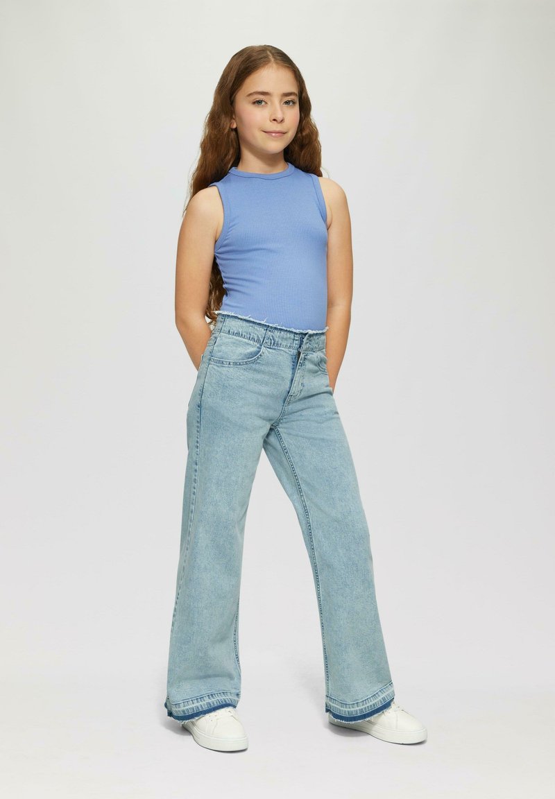 Top azul sin mangas de canalé combinado con jeans de pierna ancha azul claro. Los jeans tienen un dobladillo deshilachado y un ajuste relajado; unas zapatillas blancas completan el conjunto.