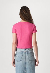 Roosa, lühikeste varrukatega ribakujuline pluus, millel on ümar kaelus ja laineline äär. Kombineeritud heledast sinisest denimis seeliku ja tooni järgi.