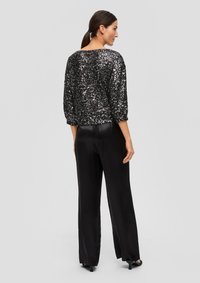 Schwarzes, mit Pailletten besetztes Oberteil mit Dreiviertelärmeln, kombiniert mit schwarzen, satinierten, weiten Hosen. Das Outfit zeichnet sich durch eine glatte Textur und eine lockere Passform aus.