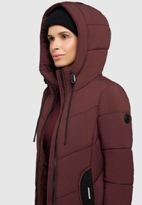 Burgunderfarbene Daunenjacke mit abnehmbarem Kapuze, Reißverschluss vorne, schwarzen Kordelzügen und seitlichen Taschen mit schwarzen Akzenten und Logodetails.