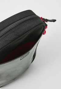 Borsa nera con zip e un'esterno testurizzato, foderata in rosso, con zip evidenti. Presenta una forma elegante e arrotondata.