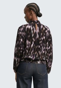 Langärmlige Bluse aus einem plissierten Stoff mit einem schwarzen, lila und braunen abstrakten Muster, mit einem Schlüssellochausschnitt auf der Rückseite und einem elastischen Saum.