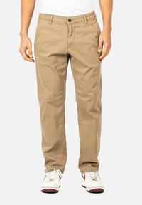 Khakifarbene Chinos aus Baumwolle mit geradem Schnitt, ausgestattet mit einem Knopfverschluss, Gürtelschlaufen und seitlichen Taschen; kombiniert mit weißen Sneakers.