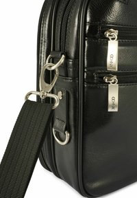 Czarna skórzana torba z wieloma kieszeniami na suwak, srebrnym okuciami i teksturowanym wykończeniem. Zawiera odpinany pasek na ramię z taśmy.