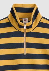 Pull jaune et bleu foncé à rayures horizontales avec une fermeture éclair à moitié sur le devant et un col montant, présentant un petit "LS" brodé sur la poitrine.