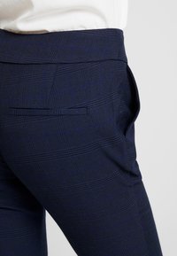 Námořnické kárované kalhoty s texturovaným vzorem, která mají zadní kapsu a úzký střih. Látka má hladký povrch a jemný lesk.