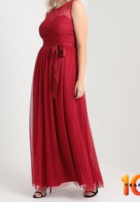 Lång röd klänning av genomskinligt tyg med en tajt bodice, flödande kjol och en knuten midjedetalj. Har en rund halsringning och är ärmlös.