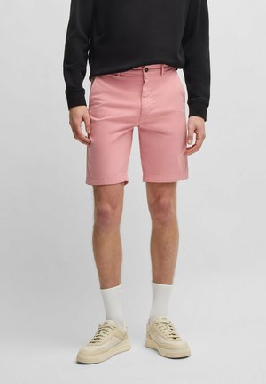 Pantalones cortos de algodón rosa con un frente plano, bolsillos laterales y detalle en el bolsillo trasero. Combinados con un sudadera negra y zapatillas beige.