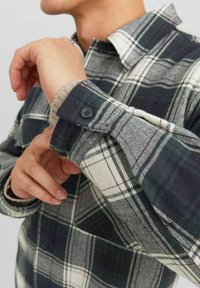 Cămașă cu carouri în nuanțe de verde închis, alb și gri. Are mansete cu nasturi, căptușeală contrastantă și un design clasic al gulerului.