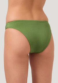 Bas de bikini vert avec une texture lisse, un design échancré et une couverture arrière minimale. Présente une taille qui repose à plat contre le corps.
