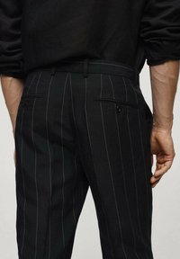Pantaloni neri su misura con sottili righe verticali, realizzati in tessuto liscio, dotati di tasche laterali e passanti per la cintura.