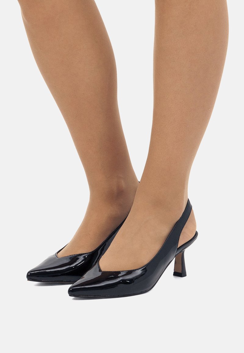 Zapatos de tacón con tiras de charol negro, diseño minimalista, tacones bajos y cuadrados, y laterales ligeramente transparentes.