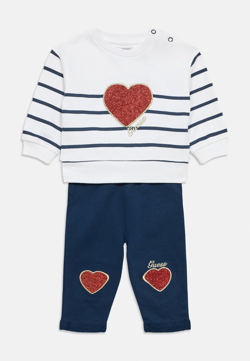 Άσπρο φούτερ με ναυτικό ρίγες, κόκκινο πατς καρδιά με γκλίτερ και λογότυπο "Guess". Σκούρο μπλε παντελόνι με δύο ταιριαστά πατς καρδιά και κέντημα.