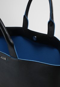 Czarna torba na ramię z niebieskimi akcentami, wykonana z teksturowanego materiału. Wnętrze jest jednolicie niebieskie, z zapięciem na zatrzask i dwiema solidnymi rączkami.