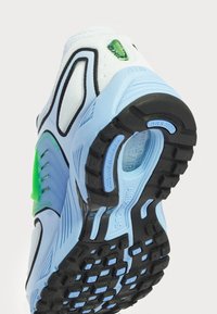 Scarpa sportiva azzurro chiaro con tomaia in mesh, dettagli verdi e suola in gomma nera con texture. Cuciture distintive e marchio ben visibili.