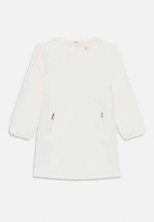 Hvit kjole med lange ballongsleeves, teksturert stoff og to frontlommer med glidelås. Rund hals med liten sløyfe til lukking bak.