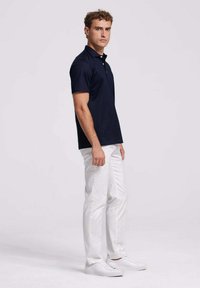 Marineblauw poloshirt met korte mouwen en kraagontwerp. Gecombineerd met witte broek en witte sneakers, tegen een effen achtergrond.