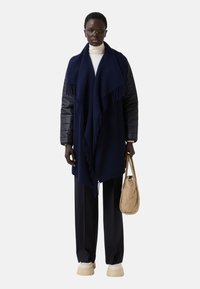 Námořnický modrý šál s třásněmi, nošený přes světlý rolák, doplněný tmavými kalhotami a prošívanou béžovou taškou. Masivní bílé boty.