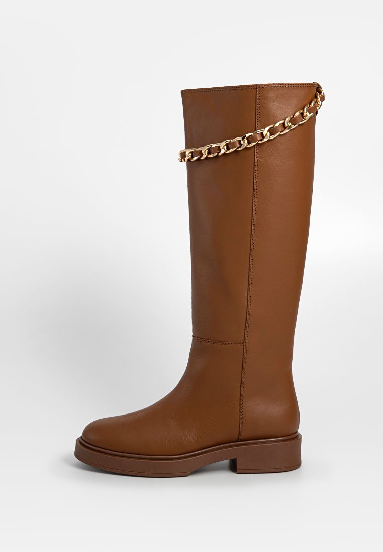 Bruin leren kniehoog laars met een platte zool, voorzien van een gouden kettingaccent aan de bovenkant, slank ontwerp en een gladde textuur.